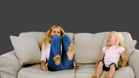 mother and daughter jumping on the sofa on grey background