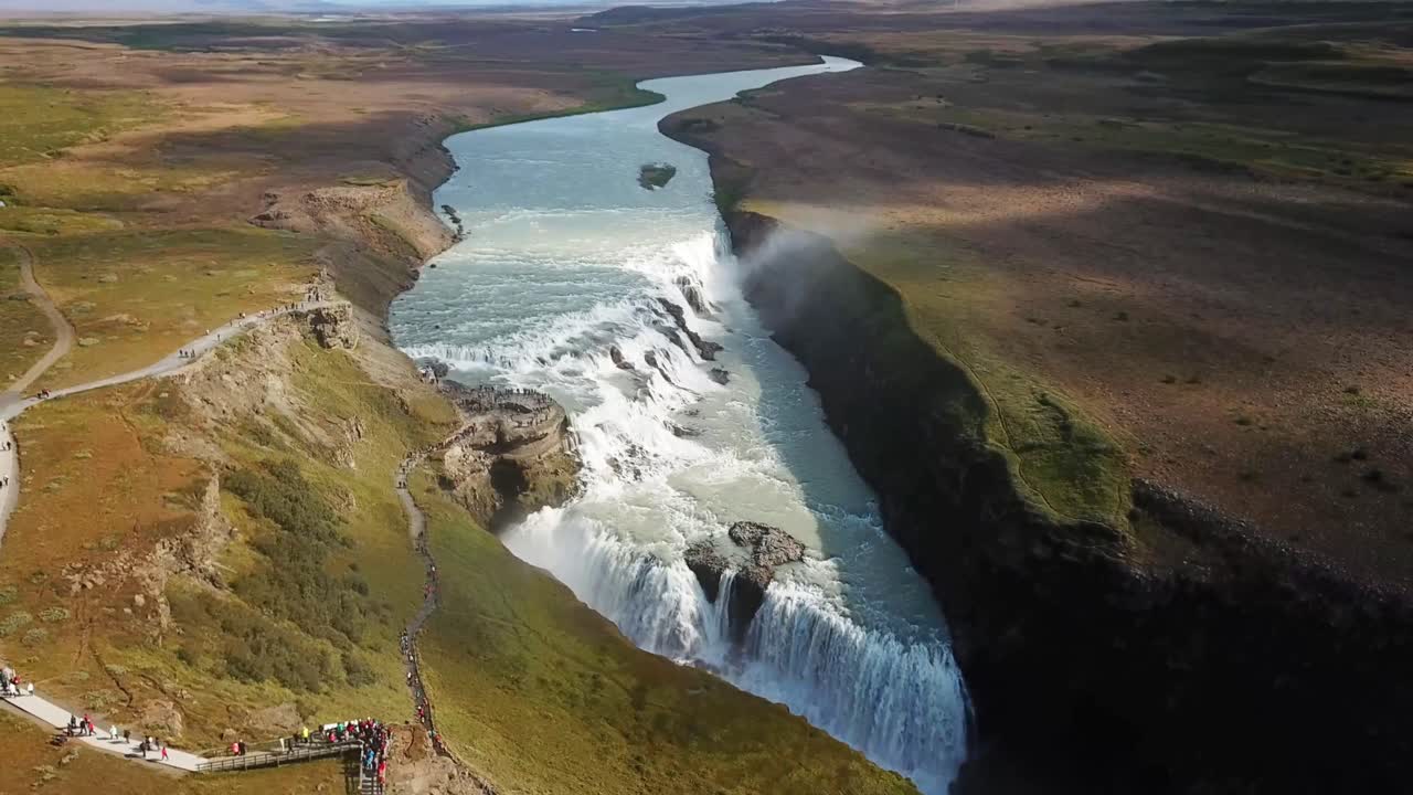 A breathtaking aerial view of Gullfoss waterfall in Iceland, where powerful cascading water flows into a rugged canyon surrounded by vibrant terrain, a prominent feature in the Golden Circle