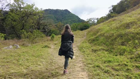 A-girl-walking-on-a-mountain-road,-surrounded-by-breathtaking-views-of-the-mountains-and-valleys