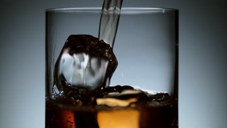 corriente de licor que fluye en el vidrio con cubitos de hielo