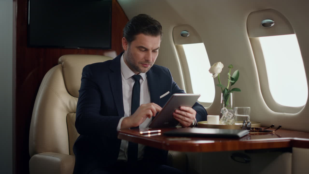 Manager nervoso che tiene un tablet su un jet di lusso. Uomo concentrato che guarda il tablet