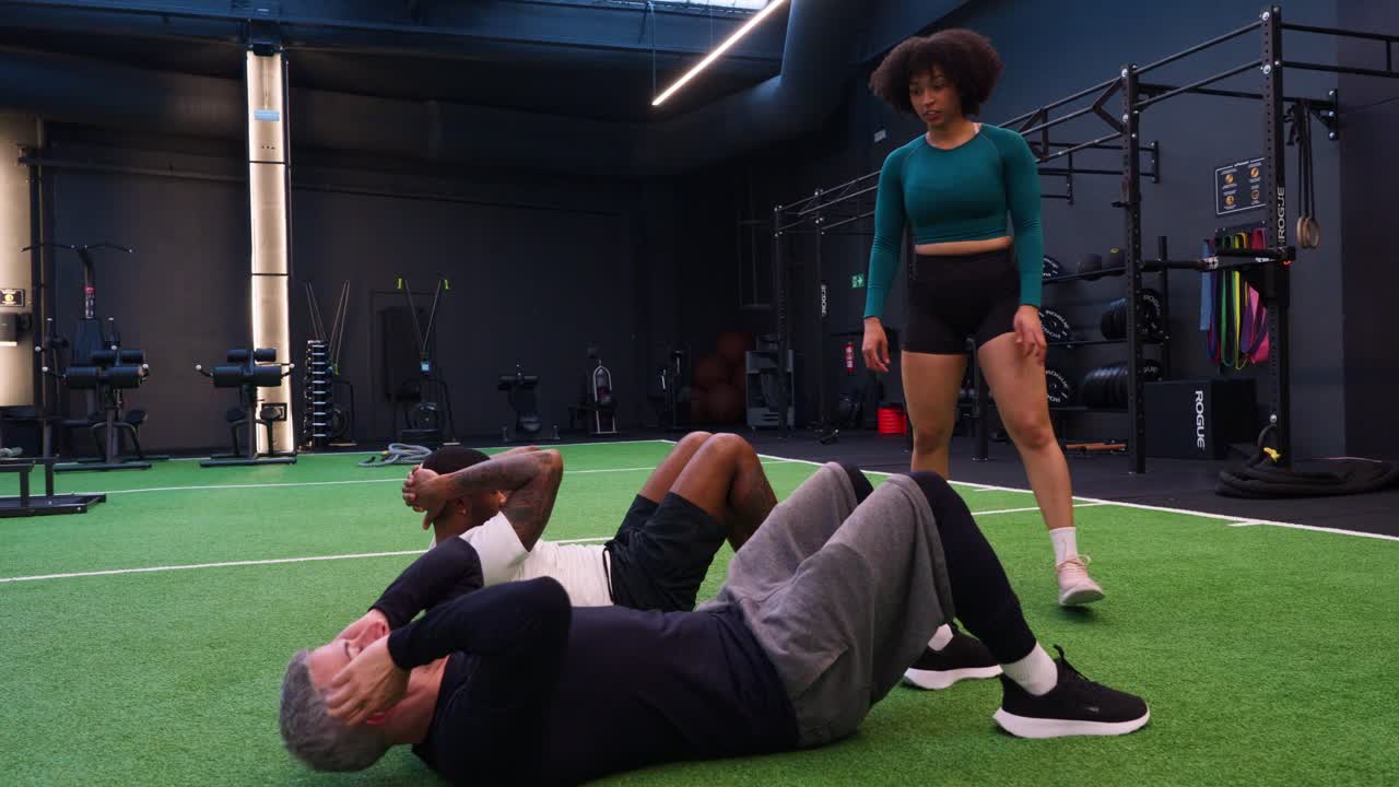 To mænd laver sit-ups med en kvindelig træner i et moderne fitnesscenter.