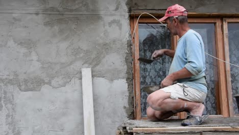 a hardworking man places cement on the window ledge on the outside of his house