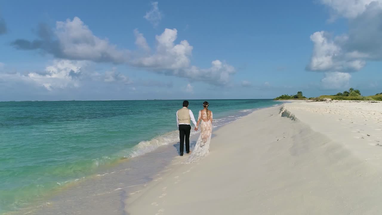 COUPLE WEDDING DRESSED WALK ON WHITE SAND BEACH WETTING FEET, CAYO DE AGUA ISLAND Los Roques