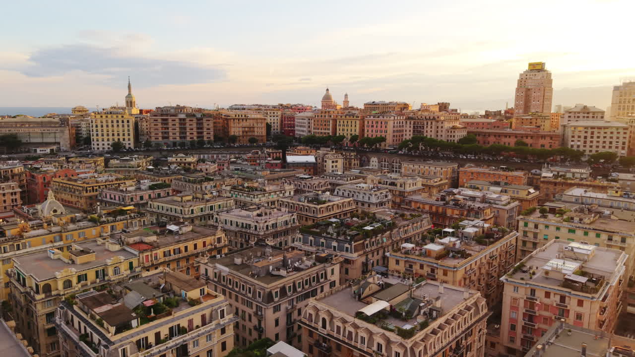 Drone flight over Genoa rooftops at sunset, showing uniform buildings, distant hills, and golden evening light