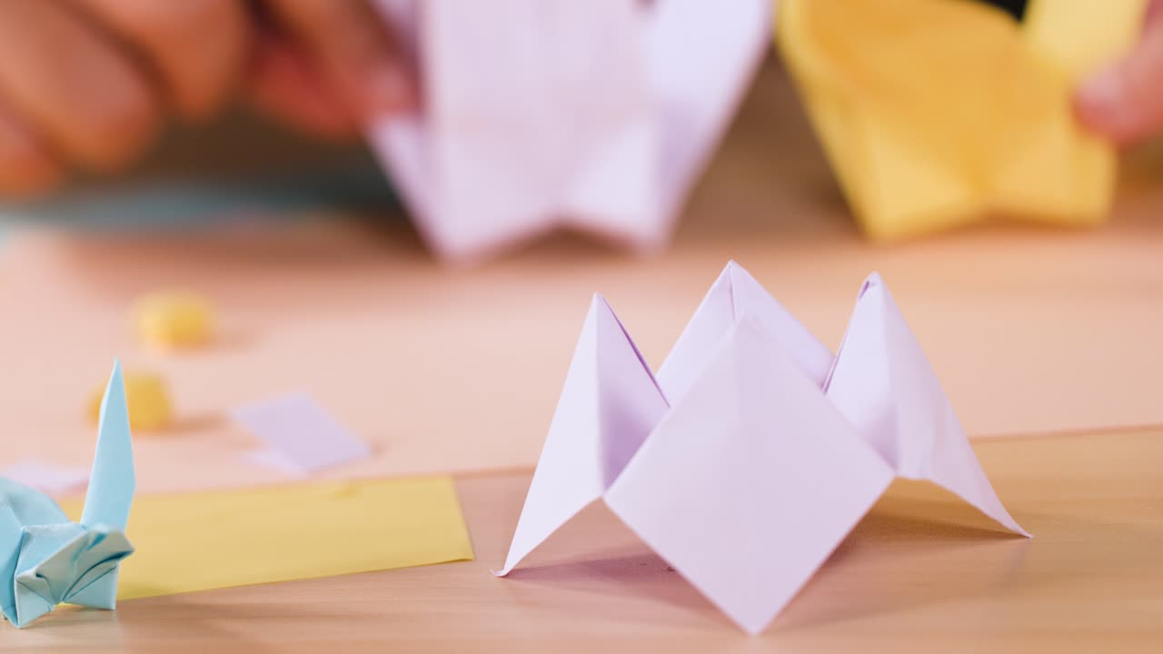 Mani piegano delicatamente la carta creando figure origami su un tavolo di legno con una tenue illuminazione naturale