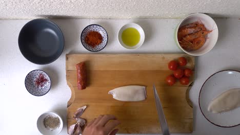 overhead view of male hands taking and cutting squid tube for paella