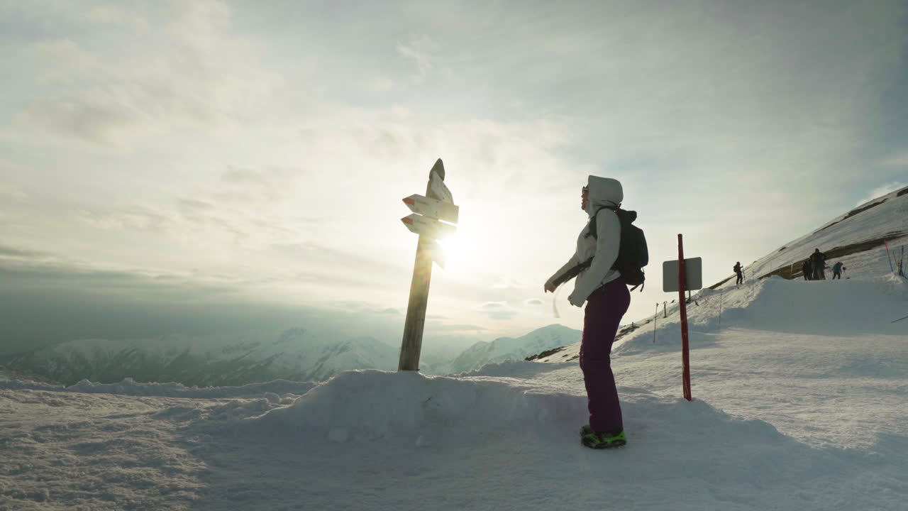 Hiker woman looking at a sign on a snowy mountain under the sunlight