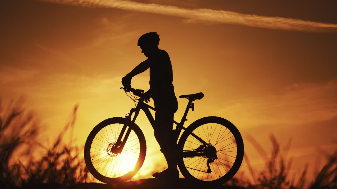 Silhouette of a biker with his bike walks outdoors at sunset. Healthy cyclist walking in the evening and a man's silhouette going by against the beautiful summer sunset.