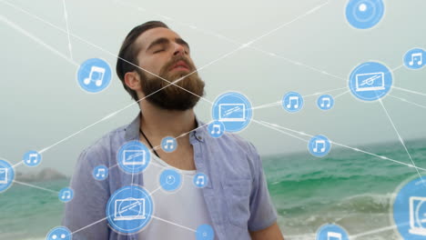 red de iconos digitales contra el hombre caucásico con los ojos cerrados de pie en la playa