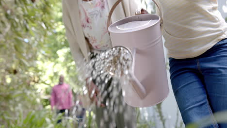 Happy-african-american-grandmother-and-granddaughter-watering-plants-in-sunny-garden,-slow-motion