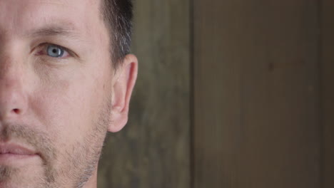 half-face-close-up-portrait-of-young-handsome-man-looking-at-camera-serious-blue-eyes-caucasian-male-on-wooden-background