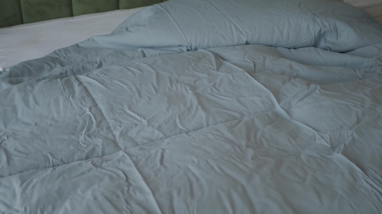 Close-up of a neatly made bed with a blue duvet, white sheets, and a green headboard