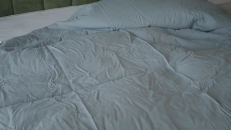 close-up of a neatly made bed with a blue duvet, white sheets, and a green headboard