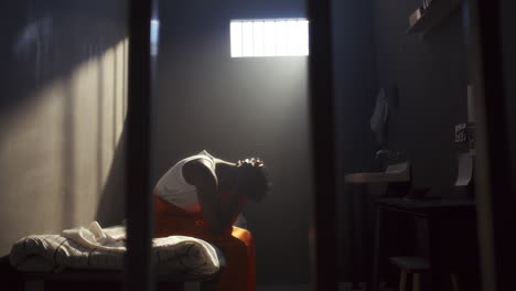 view through bars of inmate sitting on prison bed with head in hands