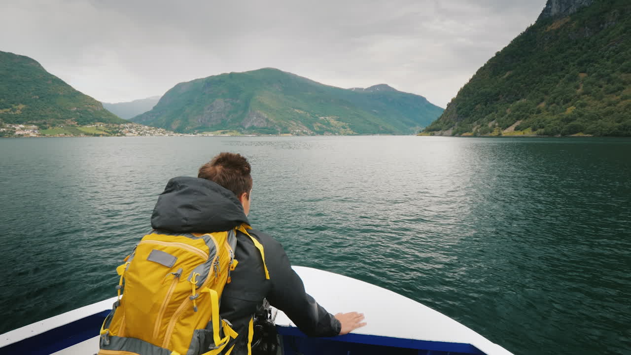 un homme avec un sac à dos voyage à travers un fjord pittoresque en norvège debout sur la proue du navire