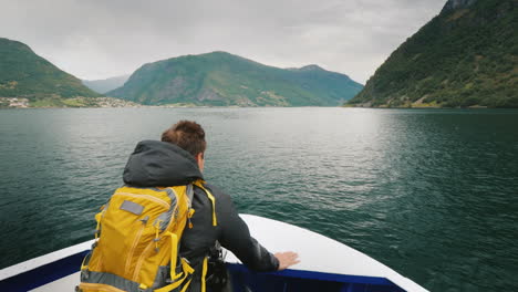 a man with a backpack travels through a picturesque fjord in norway standing on the bow of the ship