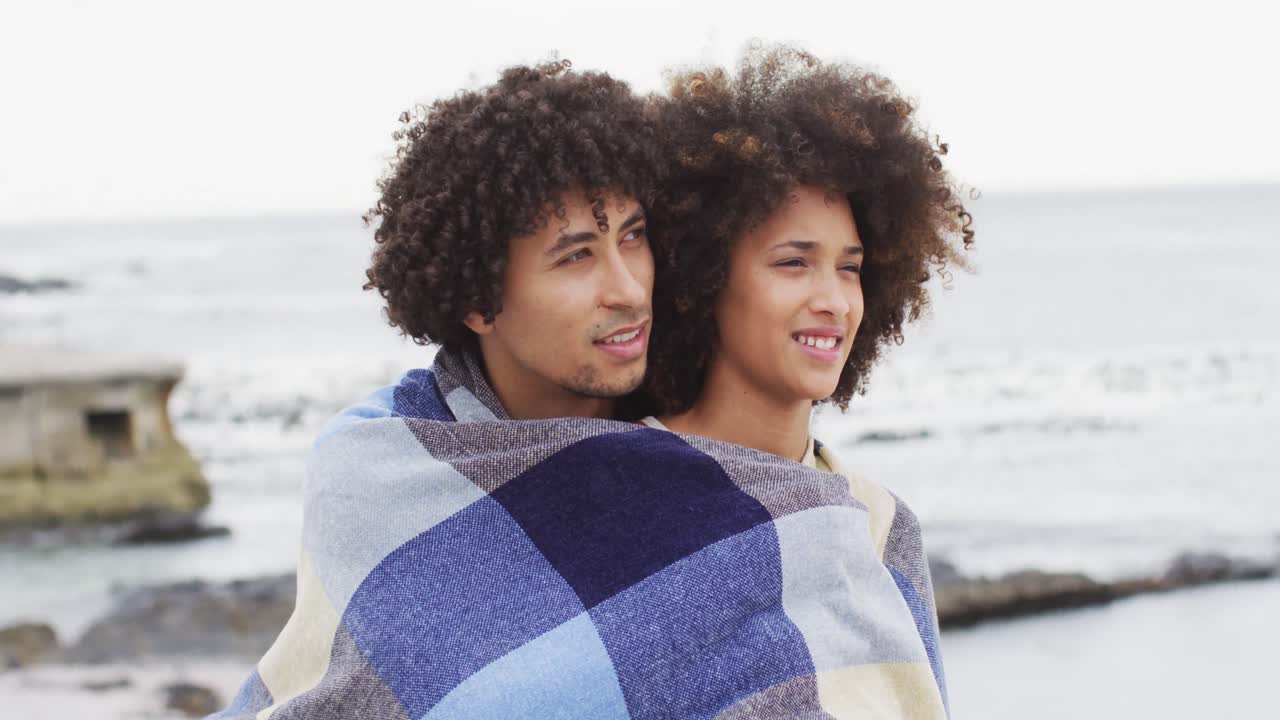 African american couple wrapped in blanket on the promenade near the beach