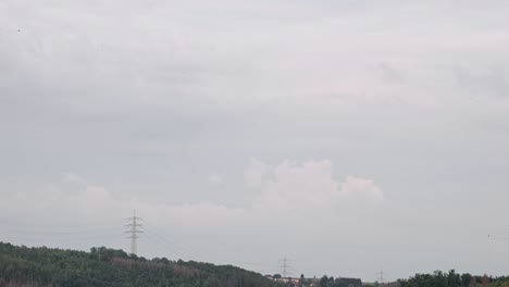 Dicke-Gewitterwolken-Ziehen-Am-Horizont-Vorbei,-In-Der-Ferne-Sind-Nadelbäume-Und-Stromleitungen-Zu-Sehen