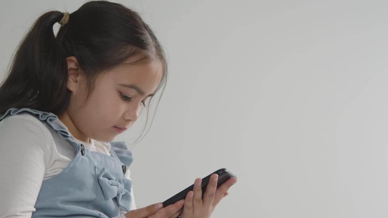 Studio Close Up Of Young Girl On ASD Spectrum Gaming On Mobile Phone Against White Background 1