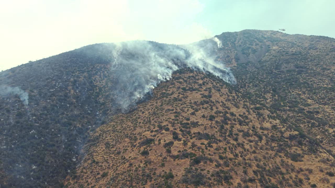 Ampia vista aerea cinematografica con drone di un incendio che brucia lungo una cresta montuosa, con un elicottero in funzione in lontananza sulle Ande, Cile, video 4K