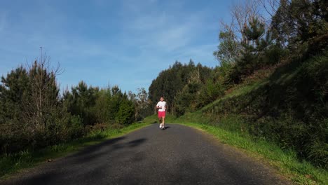 athlete running on the concrete road through dense nature. tracking pullback shot
