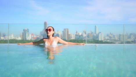 sexy lady leaning on the edge of a rooftop infinity pool, a beautiful young woman enjoys the sun and water with bangkok city skyline behind her, thailand urban vacation