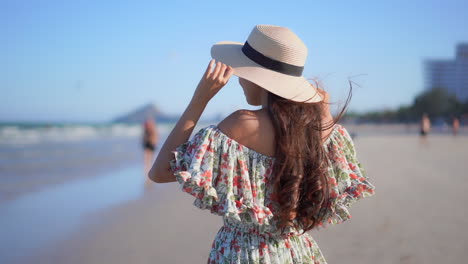 vista trasera de una mujer sosteniendo un sombrero debido a un fuerte viento en la playa