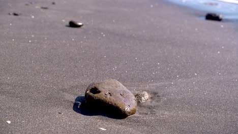 slow motion view of single rock on sandy beach with small waves breaking in distance