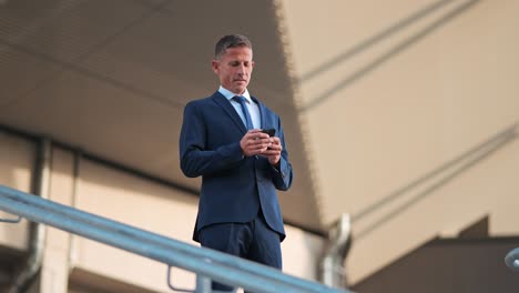 orbit low-angle shot of a mature businessman in a suit standing on the top of stairs making a call