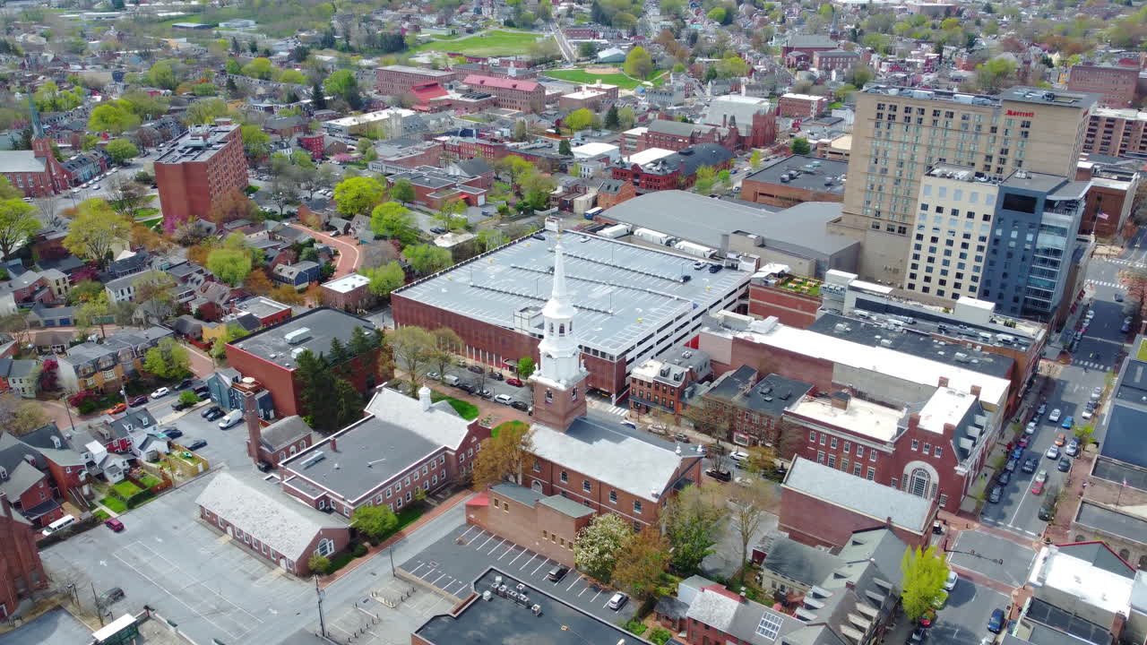 A rotating drone shot circles a white-steepled historic church in the heart of Lancaster City, PA. Spring trees and brick architecture highlight the small-town charm and rich history of the area.