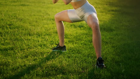 a young woman performs a static exercise on the grass for the leg and hip muscles. to rise on toes while sitting. exercise for the lower leg. training on the street in the park