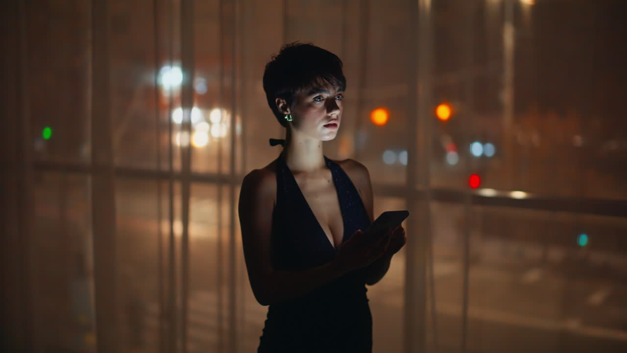 Velhavende kvinde browser smartphone ved vinduet om natten i en lejlighed, nærbillede. Melankolsk kvinde.