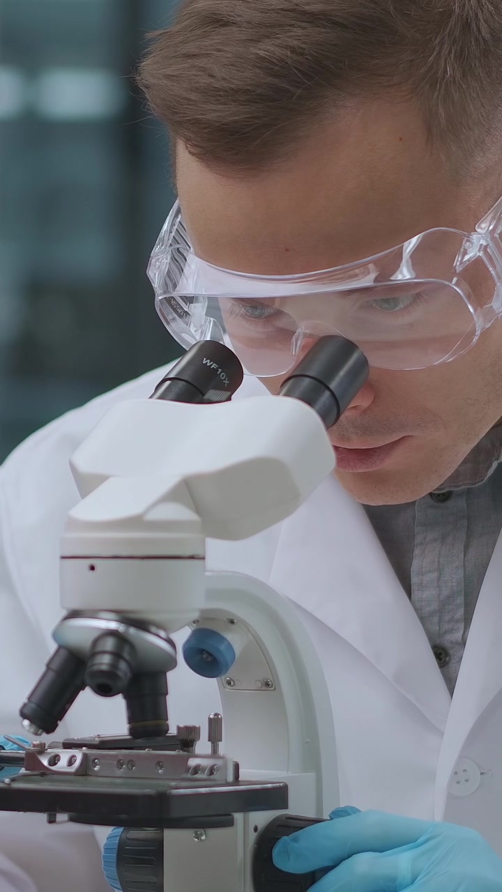 Male Scientist in Lab Coat Looking Through a Microscope