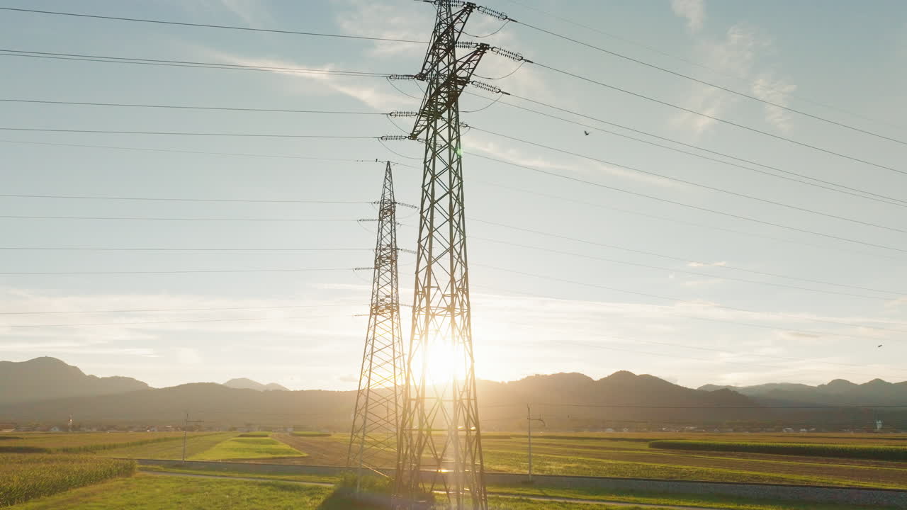 Power lines and towers are visible in a rural area as the sun sets in the background highlighting