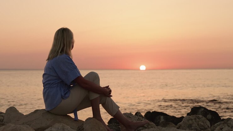 Woman watching the sunset on a rocky beach