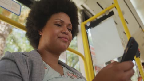 mujer biracial feliz de talla plus usando un teléfono inteligente en el autobús