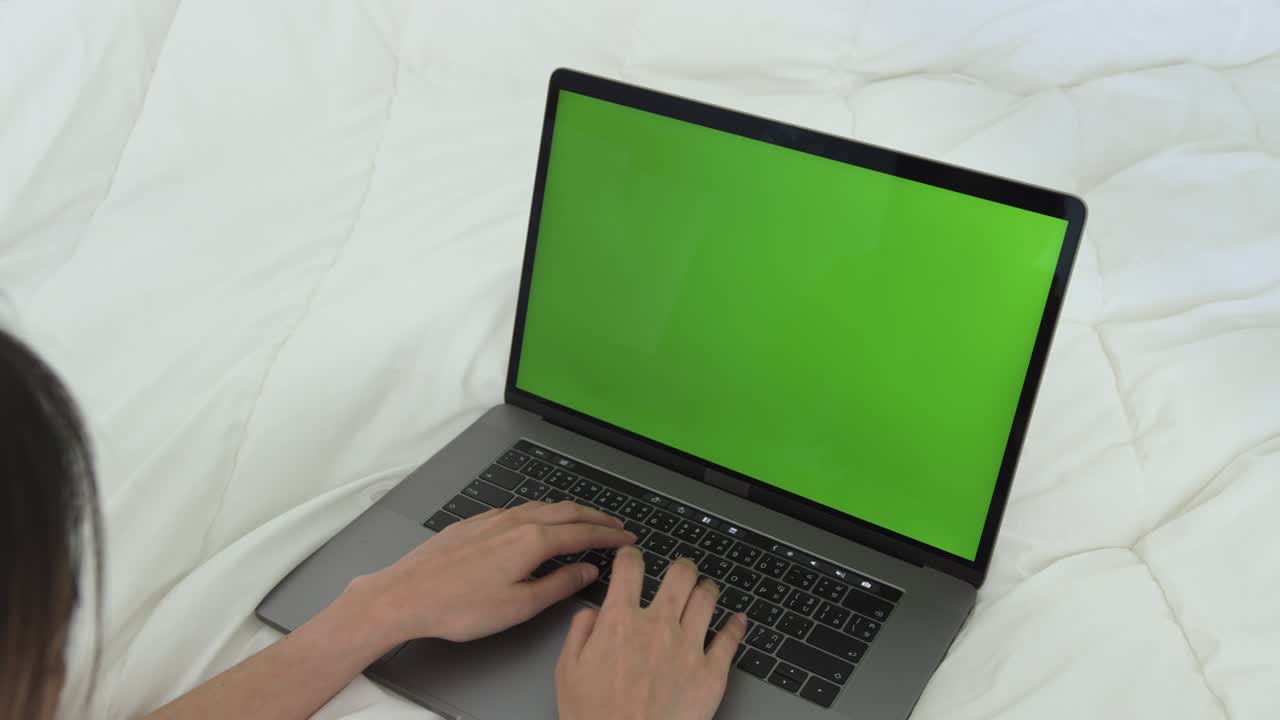 Woman using laptop with looking at green screen on the bed at home.