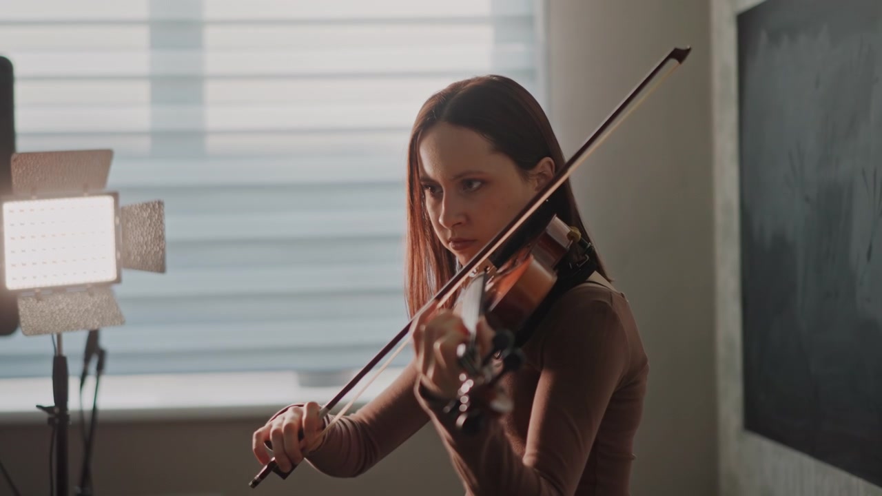 Young white violinist practicing indoors sunlit studio, focused student posture, bowing across strings, window backlight, warm cinematic lighting, teacher absent, schoolroom atmosphere