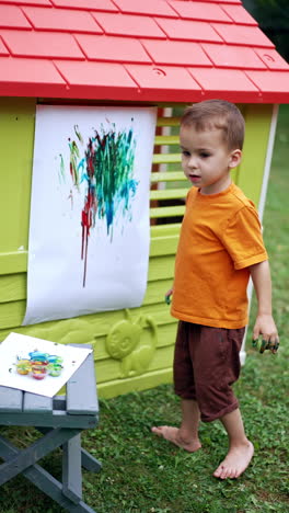 lovely little boy paints outdoors in summer. kid creates a picture using paints and his fingers only. vertical video.