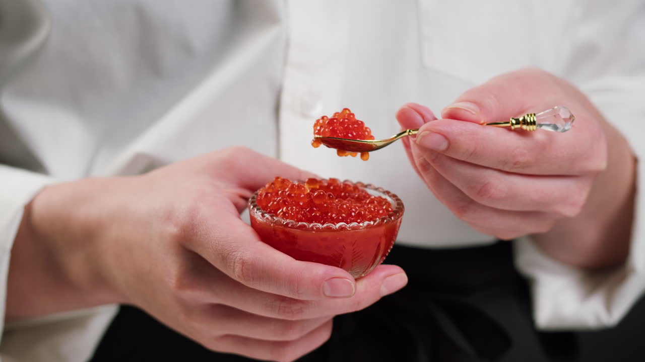 Gros plan sur des mains prélevant du caviar rouge dans un petit bol