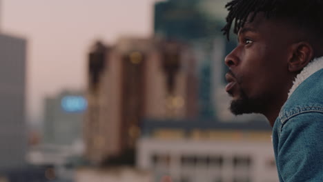 attractive young african american man drinking alcohol enjoying rooftop view of city skyline looking contemplative at sunset