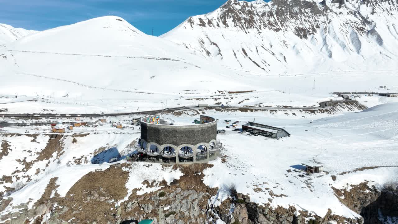 A round building stands resilient in a snowy mountain landscape, blending architectural uniqueness with the ruggedness of the alpine terrain