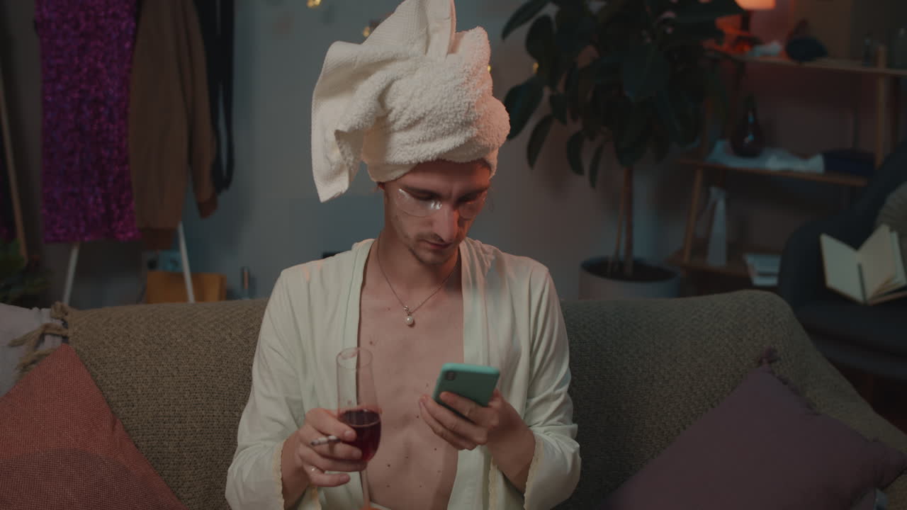 Man in bathrobe and towel with phone and wine