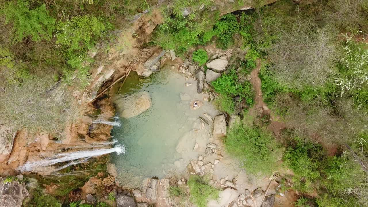vista aérea de pájaro que se eleva por encima de un joven sano admirando una cascada calmante en un paseo de ocio por la naturaleza