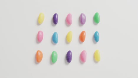 Video-of-overhead-view-of-rows-of-multi-coloured-sweets-over-white-background