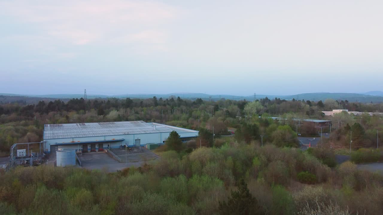 Stigende luftfoto over et nedslidt lager med læsseramper, omgivet af skovlandskab. Industriel infrastruktur omgivet af naturligt miljø. 4K.