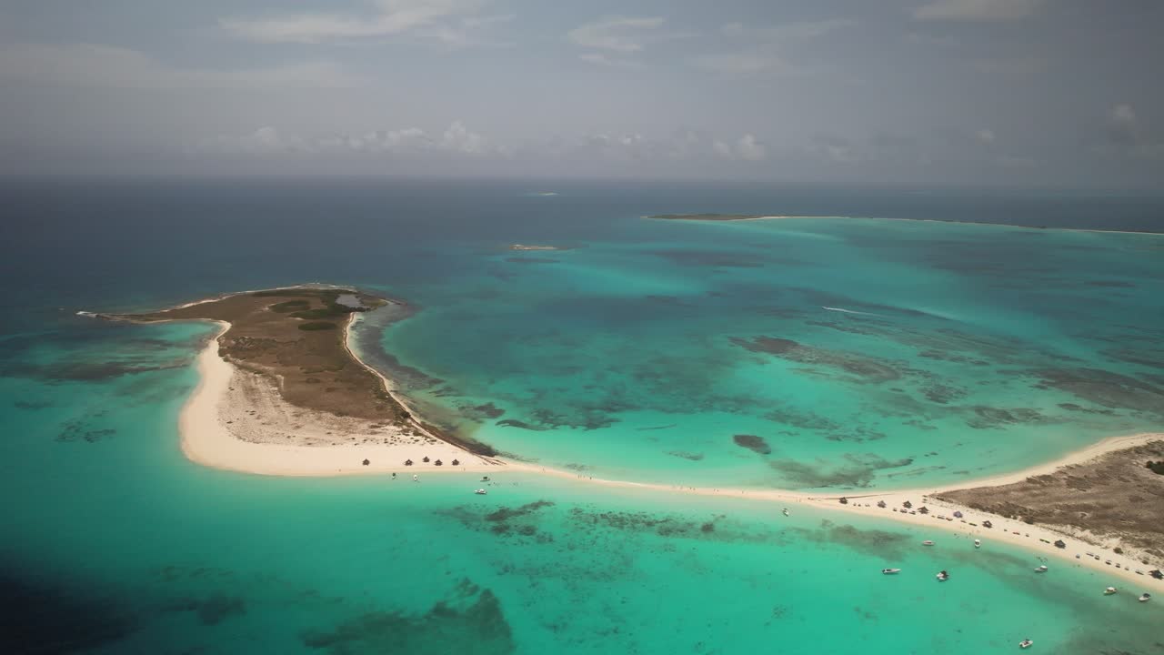una playa de arena y aguas turquesas en cayo de agua con pequeños barcos visibles, vista aérea