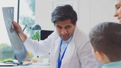 doctor in white coat with mother and son in office looking at mri or ct scans