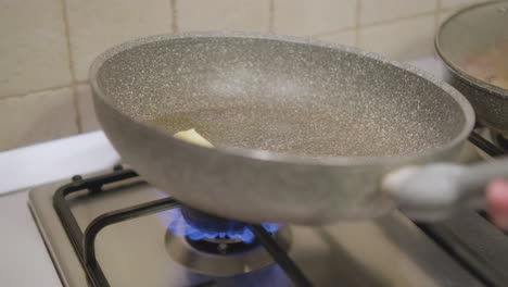 mujer sosteniendo una sartén antiadherente que se inclina para cubrir la superficie con mantequilla y aceite a fuego medio